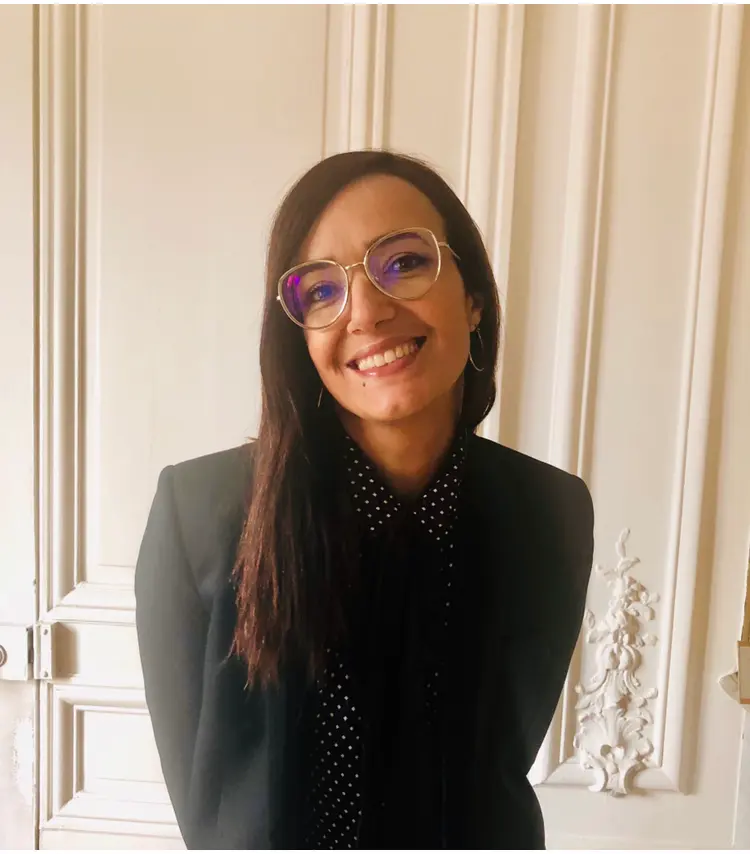Portrait de Maître Khadija Azougach, souriante, devant une porte moulurée.
